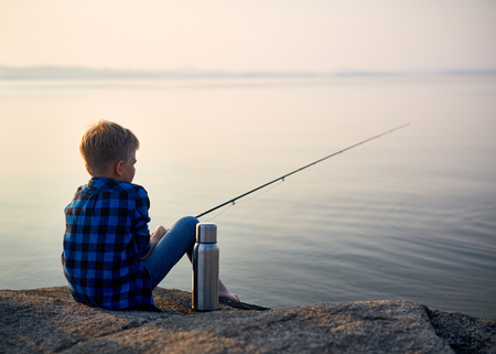 Little boy with rod waiting for fish by river