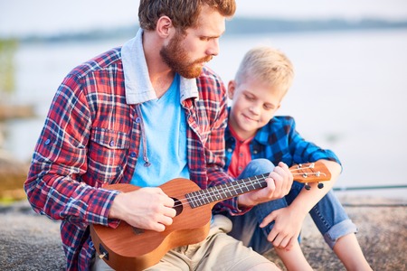 Young man showing his son how to play ukuleleの写真素材