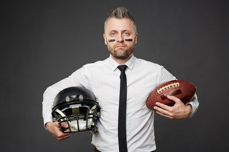 Portrait of serious man holding rugby ball and helmetの写真素材