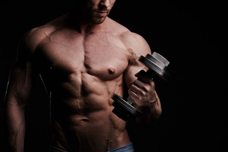 Muscular bodybuilder guy doing exercises with dumbbells over black backgroundの写真素材