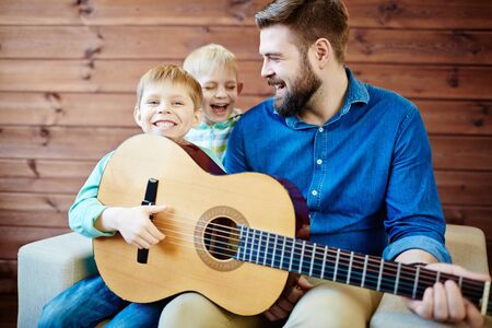 Father teaching his sons to play guitarの写真素材
