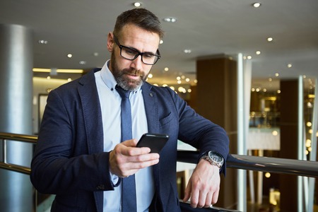 Mature businessman reading sms in business centerの写真素材