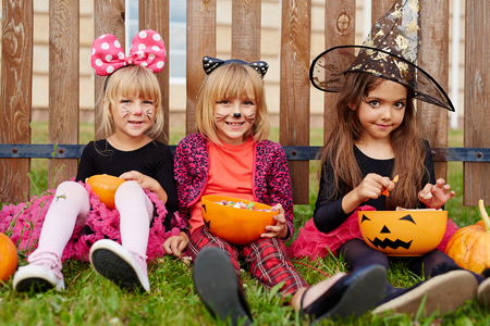 Friendly Halloween girls sitting on grass against wooden fenceの写真素材