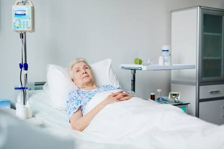 Senior female lying in bed in hospital wardの写真素材
