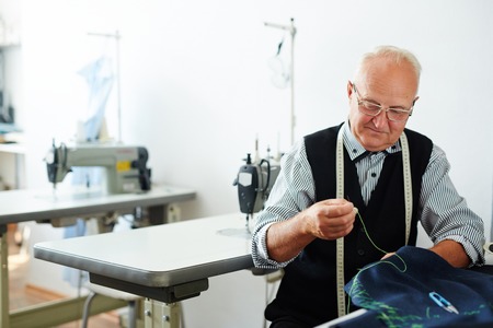 Elderly man sewing clothes in tailoring shopの写真素材