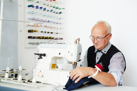 Mature tailor sewing clothes on special equipmentの写真素材