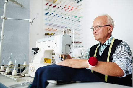 Modern tailor sitting by sewing-machineの写真素材