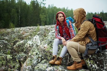 Amorous young hikers sitting on large stones during tripの写真素材