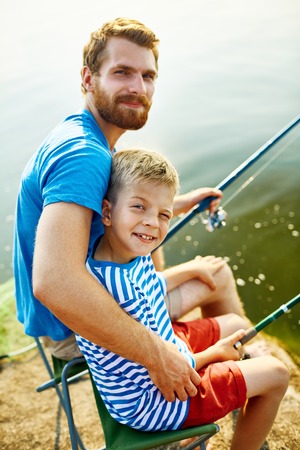 Happy young man and boy with rods looking at cameraの写真素材