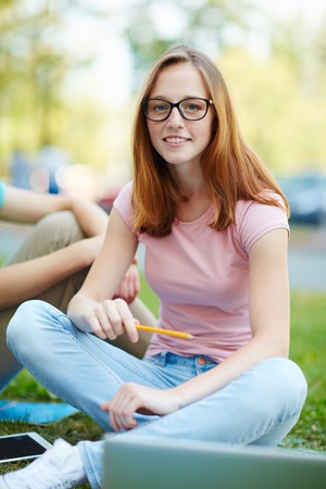 Pretty student looking at camera while sitting on lawnの写真素材