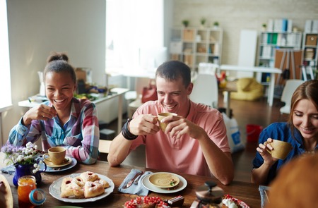 Cheerful guy and girls having tea with homemade pastryの写真素材
