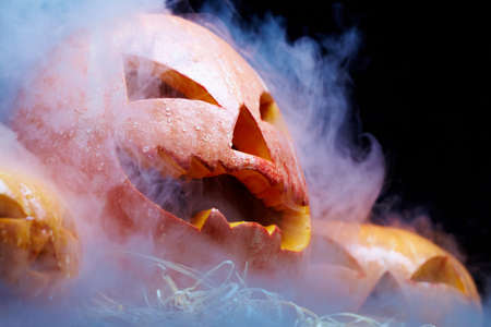 Close up of Jack O Lantern smoking among two other pumpkins against black backgroundの写真素材
