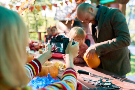 Girl taking picture of her father and sister cutting Halloween pumpkinの写真素材