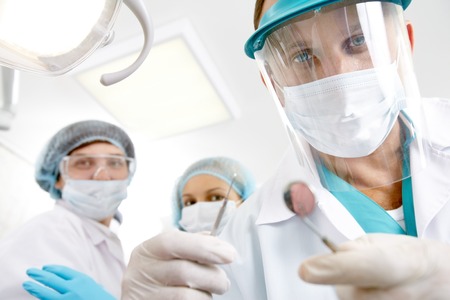 Male dentist in mask looking at camera against his colleaguesの写真素材