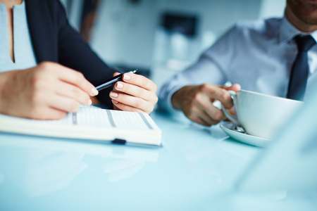 Close-up of hand of businesswoman holding a pen and her male colleague drinking coffeeの写真素材