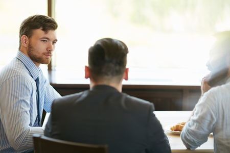 Three businessmen sitting in cafe in silenceの写真素材
