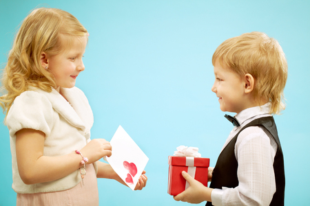 Two children standing and exchanging presents, gift for girl and post card for boyの写真素材