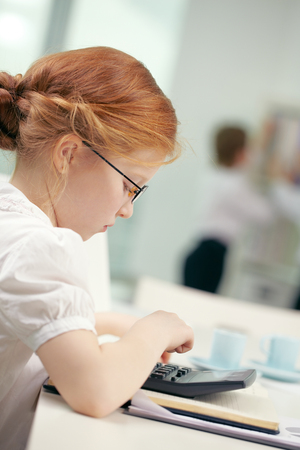 Little cute red hair student girl counting with calculatorの写真素材