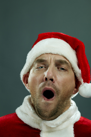 Portrait of man in Santa costume looking at camera and yawningの写真素材