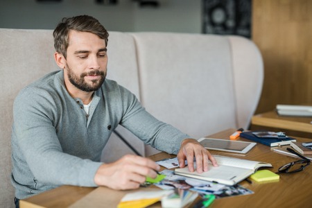 Young man with pen looking at photographs at workplace
