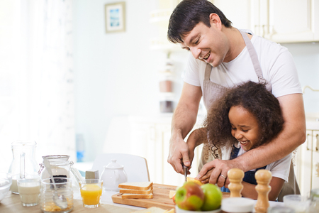 Young father showing his daughter how to cut breadの写真素材