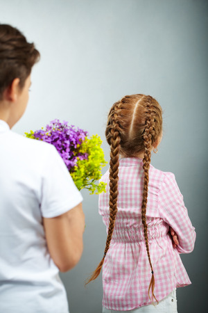A little girl turning her back to a boyfriend with flowersの写真素材