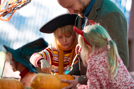 Father teaching his daughters carve a pumpkinの写真素材
