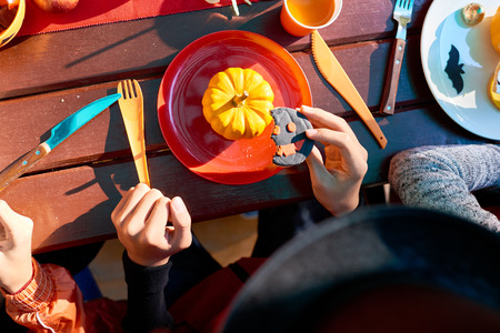 Close-up of people sitting at the table and eating cookies on Halloween partyの写真素材