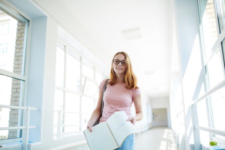 Adolescent student with copybook standing in college corridorの写真素材