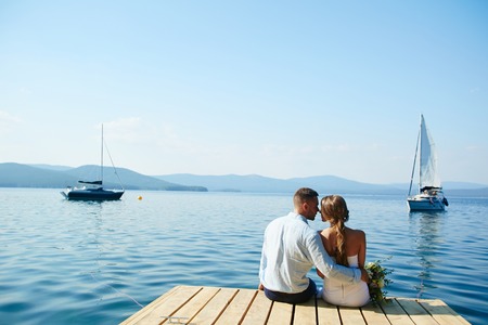 Romantic newlyweds sitting by waterの写真素材