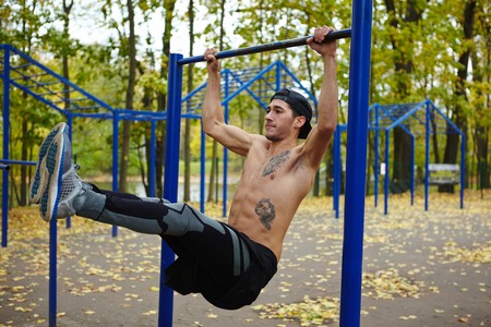 Shirtless sportsman doing pull-ups on horizontal bar