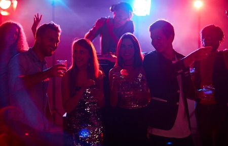 Young people with drinks talking in night club at partyの写真素材