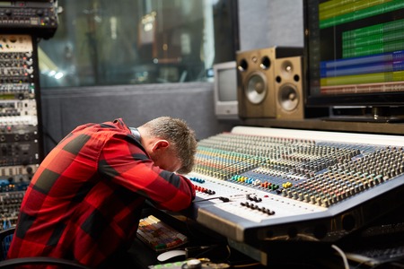 Tired deejay putting his face on soundboard in audio studioの写真素材