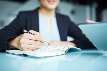 Secretary with pen holding it over open notebookの写真素材
