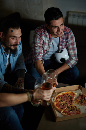 Group of fans having pizza with beer during football match broadcastの写真素材