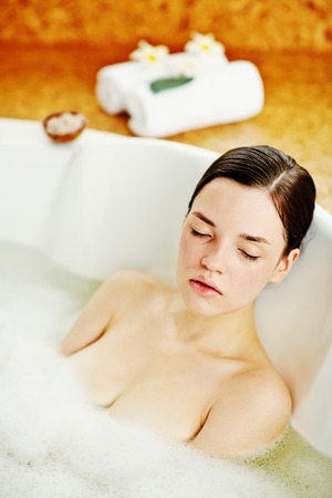 Relaxed brunette lying in bathtub with hot water and foam