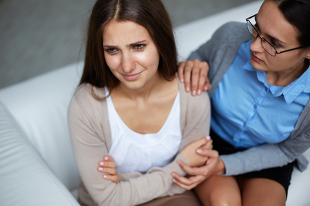 Hopeless girl weeping with psychologist reassuring herの写真素材