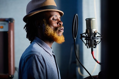 Young bearded man in hat singing in recording studioの写真素材