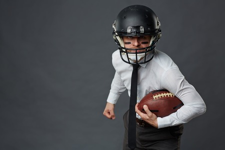 Businessman in protective helmet holding rugby ballの写真素材
