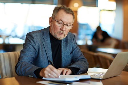 Mature business leader making notes while relaxing in cafe after workの写真素材