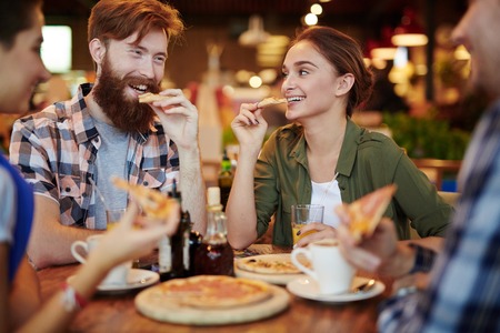 Group of friendly teens eating pizza in cafe