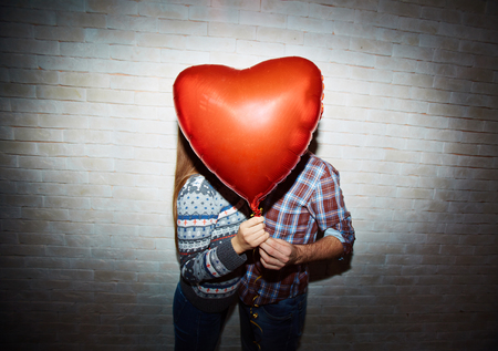 Red heart-shaped balloon and amorous couple hiding behindの写真素材