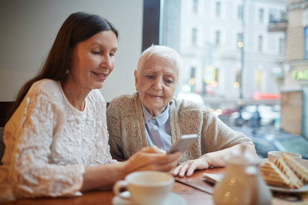 Senior females reading message in smartphone of one of themの写真素材