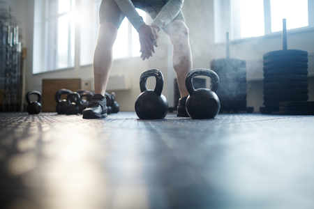 Two kettlebells on the gym floor and sportsman preparing his hands for powerliftingの写真素材