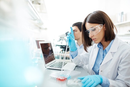 Young woman in whitecoat studying new chemical substances in lab