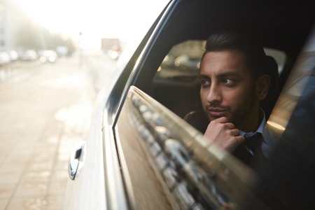 Wealthy man looking through car window while traveling in the cityの写真素材