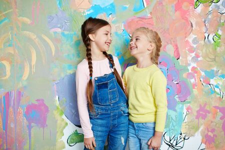 Little girls in casualwear looking at one another against creative painted wallの写真素材