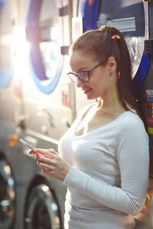 Girl with cellphone by washing-machineの写真素材