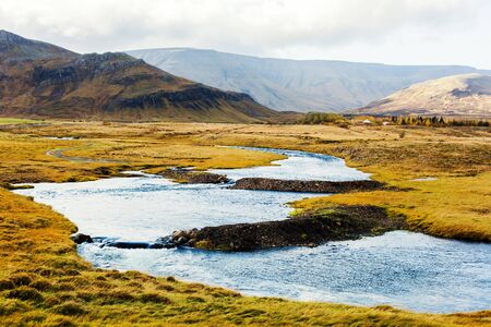 Winding river on prairie with mounts on background