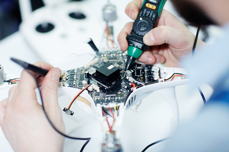 Closeup top view shot of male hands testing electric current in circuit board of disassembled drone...